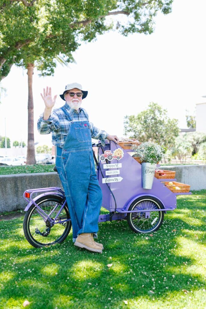 Photo by RDNE Stock project Elderly man in overalls waves by a cart in a sunny park setting.